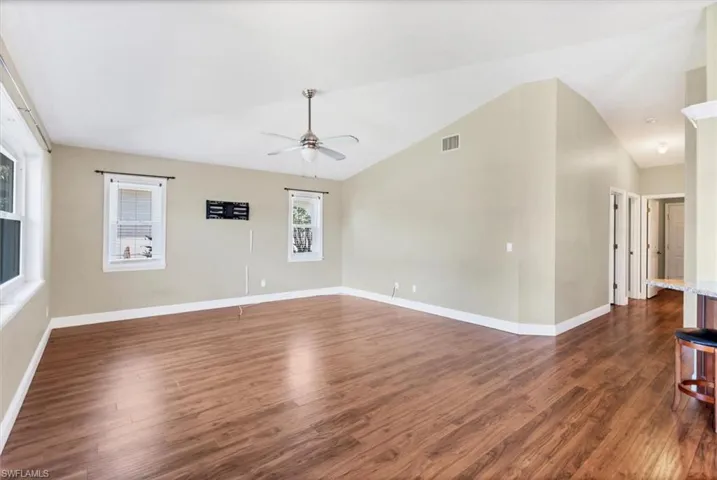 Empty room featuring ceiling fan, vaulted ceiling, a healthy amount of sunlight, and dark hardwood / wood-style floors