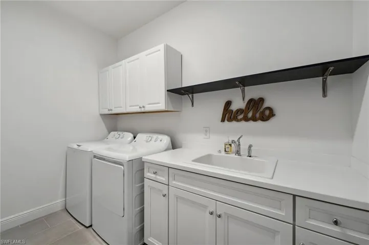Clothes washing area with washer and clothes dryer, sink, light tile floors, and cabinets