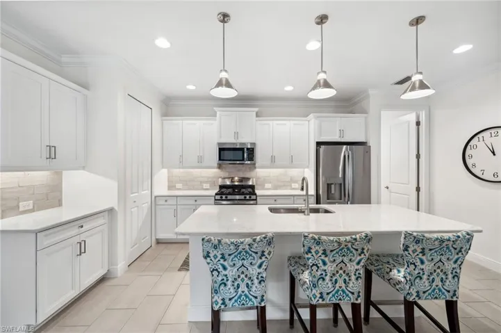 Kitchen with an island with sink, stainless steel appliances, decorative light fixtures, backsplash, and sink