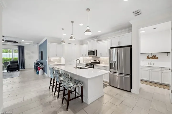 Kitchen featuring decorative light fixtures, a center island with sink, white cabinets, sink, and appliances with stainless steel finishes