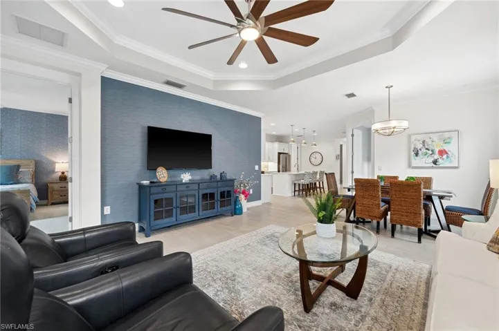 Living room featuring crown molding, a raised ceiling, and ceiling fan with notable chandelier
