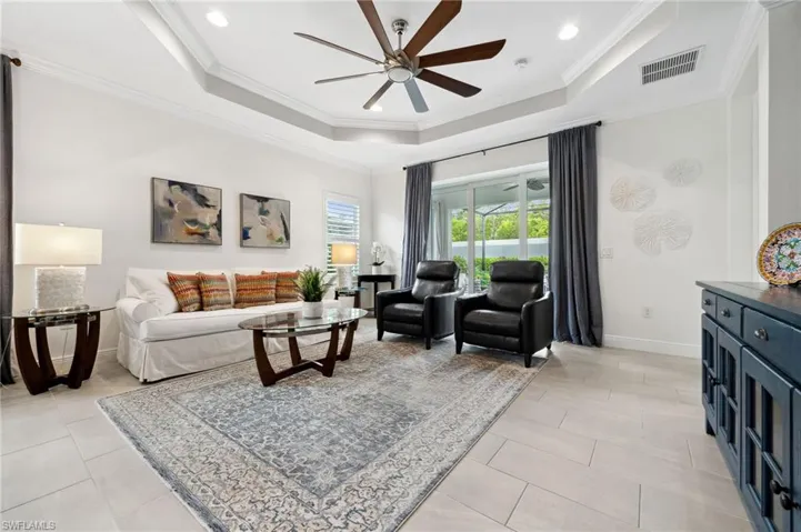 Tiled living room with a tray ceiling, crown molding, and ceiling fan