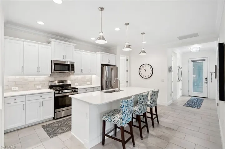 Kitchen featuring tasteful backsplash, stainless steel appliances, pendant lighting, white cabinets, and a kitchen island with sink