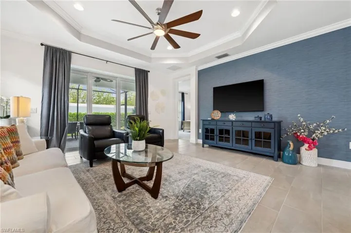 Tiled living room with ceiling fan, a raised ceiling, and crown molding
