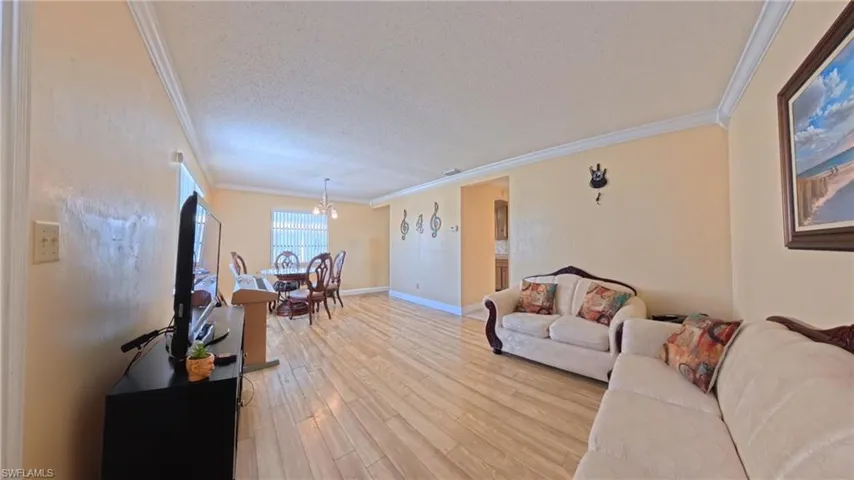 Living room featuring crown molding, light wood finished floors, a textured ceiling, and a chandelier