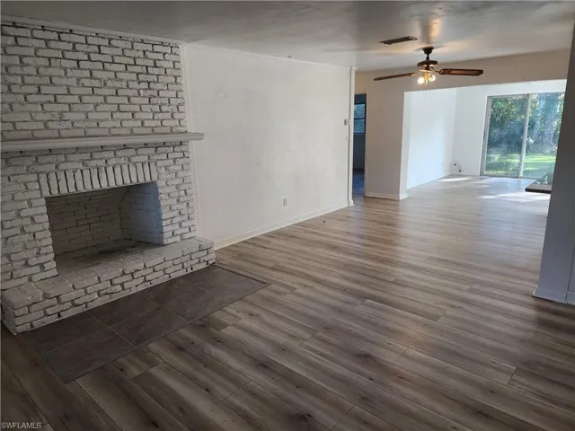Unfurnished living room featuring dark hardwood / wood-style floors, a brick fireplace, and ceiling fan