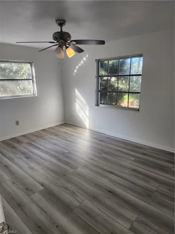 Empty room with ceiling fan, a healthy amount of sunlight, and dark hardwood / wood-style floors