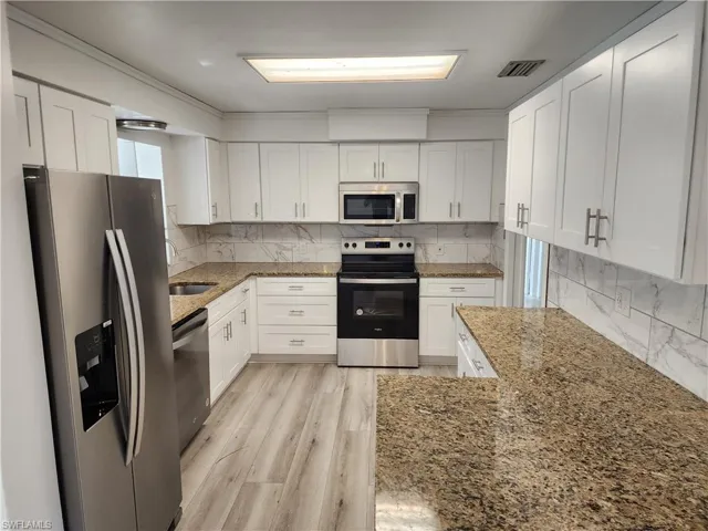 Kitchen with stone counters, white cabinetry, and stainless steel appliances