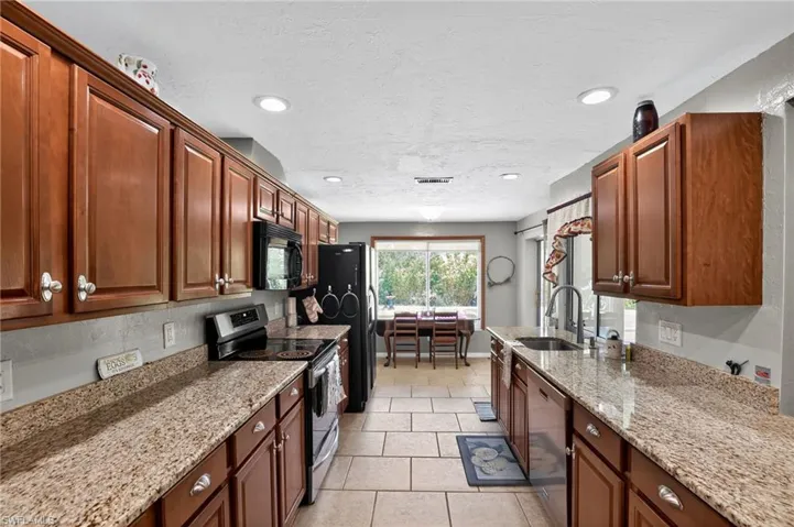 Kitchen featuring stainless steel appliances, light stone counters, a textured ceiling, light tile patterned flooring, and recessed lighting