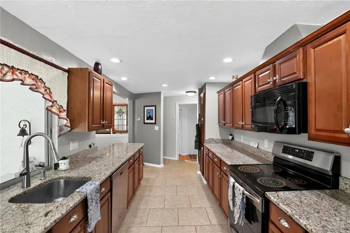Kitchen featuring appliances with stainless steel finishes, light stone countertops, recessed lighting, a textured ceiling, and brown cabinets