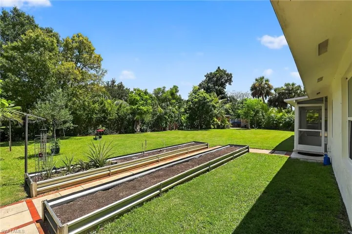 View of green lawn with view of wooded area and a sunroom