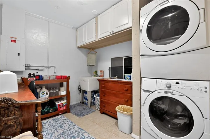 Washroom featuring electric panel, light tile patterned flooring, stacked washer / drying machine, and cabinet space