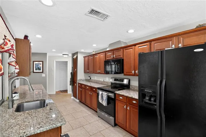 Kitchen with black appliances, light stone counters, recessed lighting, brown cabinetry, and a textured ceiling
