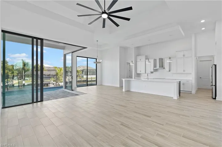 Unfurnished living room with ceiling fan, a tray ceiling, wood finish floors, and recessed lighting