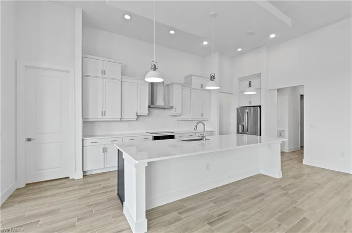 Kitchen featuring a high ceiling, white cabinetry, wood finish floors, stainless steel fridge with ice dispenser, and a kitchen island with sink