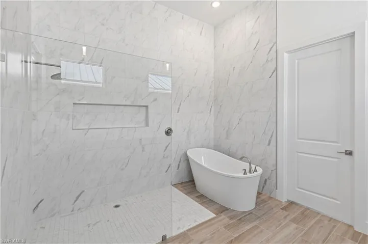 Full bath featuring a walk in shower, a freestanding tub, and tile walls