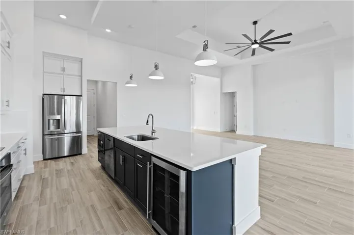 Dual tone kitchen featuring two tone color scheme, wine cooler, light stone counters, stainless steel appliances, and hanging light fixtures
