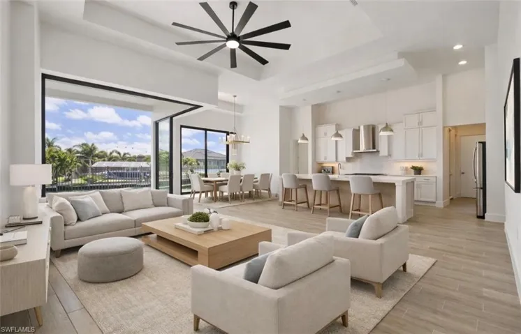Living area with wood finish floors, a ceiling fan, a raised ceiling, and a chandelier
