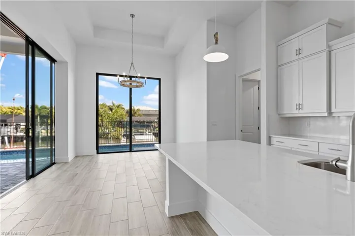 Kitchen featuring light stone countertops, white cabinets, wood finish floors, hanging lights, and tasteful backsplash