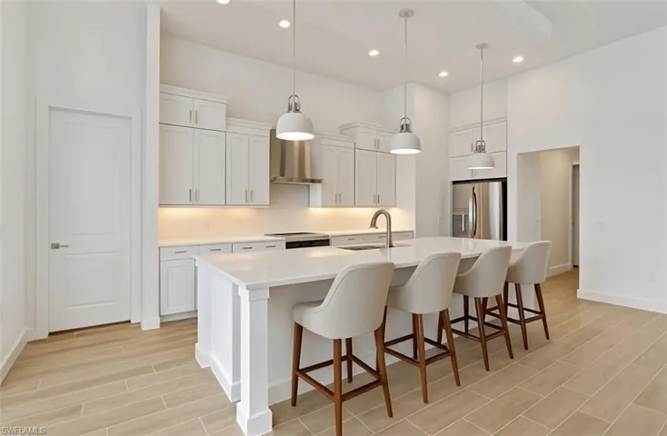 Kitchen featuring a kitchen bar, white cabinetry, stainless steel refrigerator with ice dispenser, a center island with sink, and wood tiled floors