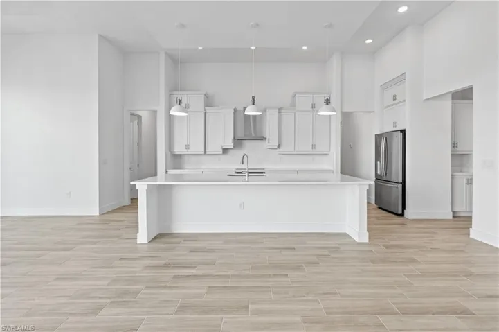 Kitchen featuring a high ceiling, white cabinets, a large island with sink, wood tiled floors, and stainless steel fridge
