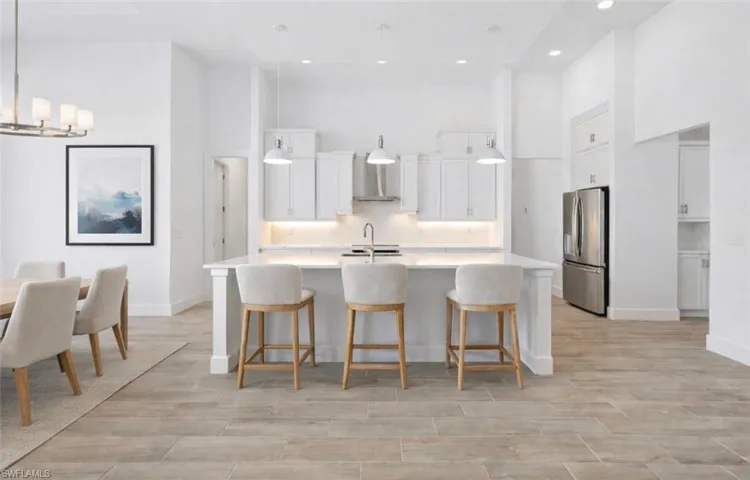 Kitchen featuring a high ceiling, white cabinetry, stainless steel refrigerator with ice dispenser, wood finish floors, and a center island with sink