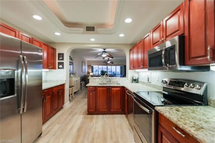 Kitchen featuring light stone countertops, stainless steel appliances, a raised ceiling, sink, and light hardwood / wood-style floors