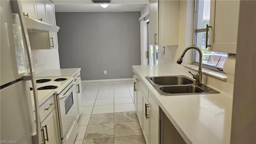 Kitchen with light tile patterned flooring, white appliances, sink, and white cabinetry