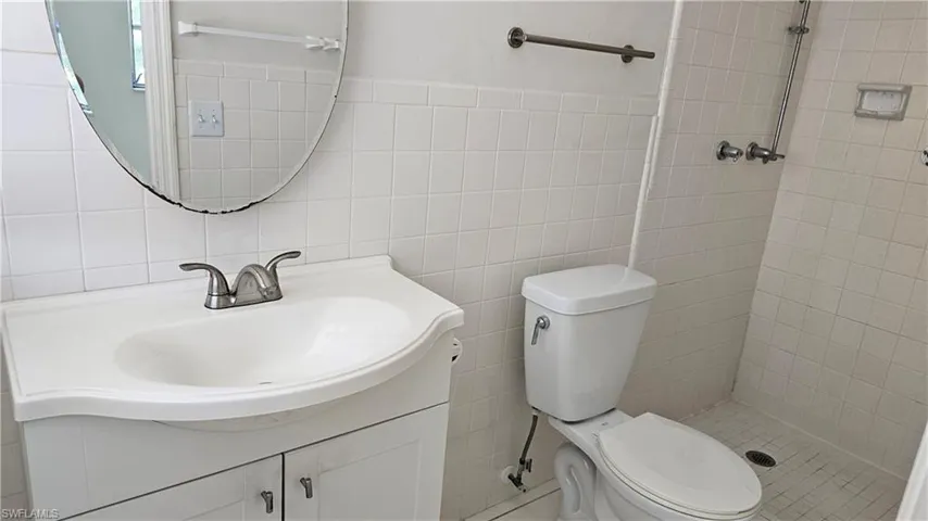 Bathroom featuring toilet, backsplash, tile walls, vanity, and tiled shower