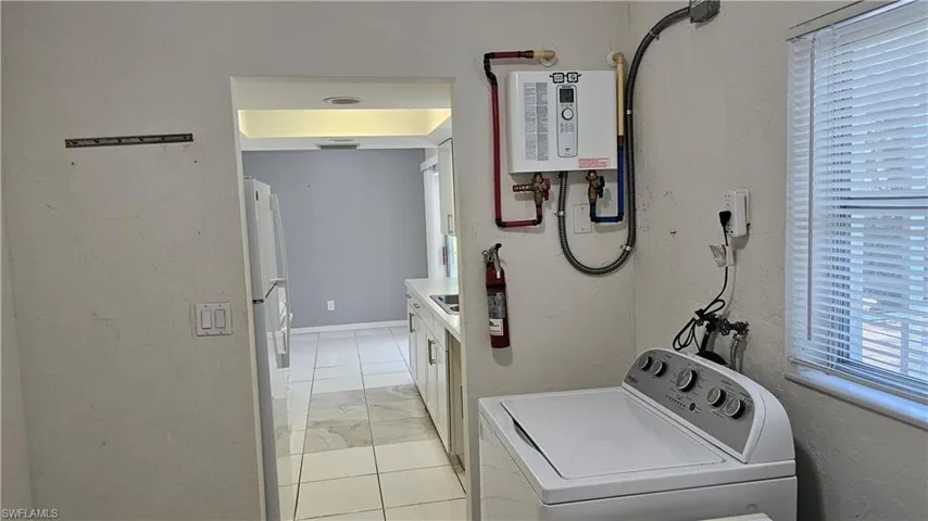 Laundry area featuring water heater, washer / dryer, and light tile patterned floors
