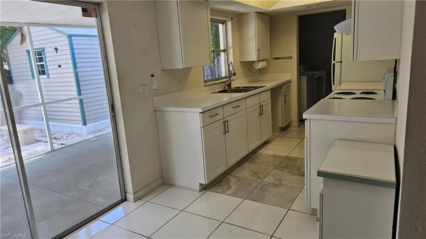 Kitchen with light tile patterned flooring, sink, stove, and washer and dryer
