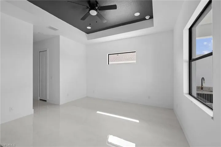 Unfurnished room with plenty of natural light, a ceiling fan, a tray ceiling, baseboards, and recessed lighting