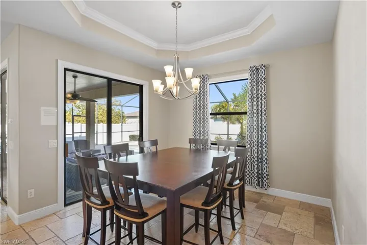 Dining room with stone tile floors, ornamental molding, a raised ceiling, ceiling fan, and a chandelier