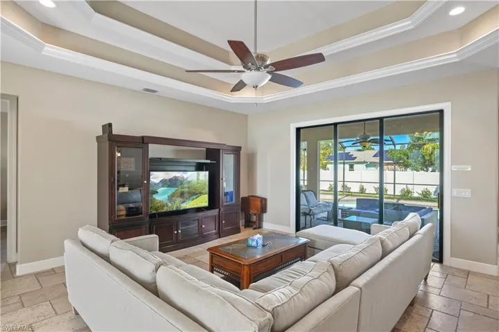 Living room featuring stone tile floors, a ceiling fan, crown molding, and a tray ceiling