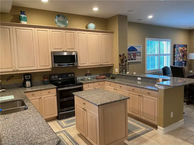 Kitchen with range with two ovens, light wood finish cabinets, stainless steel microwave, a center island, and dark stone counters