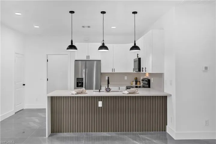 Kitchen with a peninsula, stainless steel appliances, white cabinetry, light stone counters, and a kitchen breakfast bar