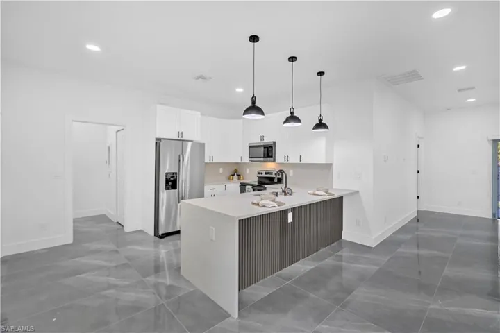 Kitchen featuring stainless steel appliances, a peninsula, decorative light fixtures, white cabinetry, and light stone countertops