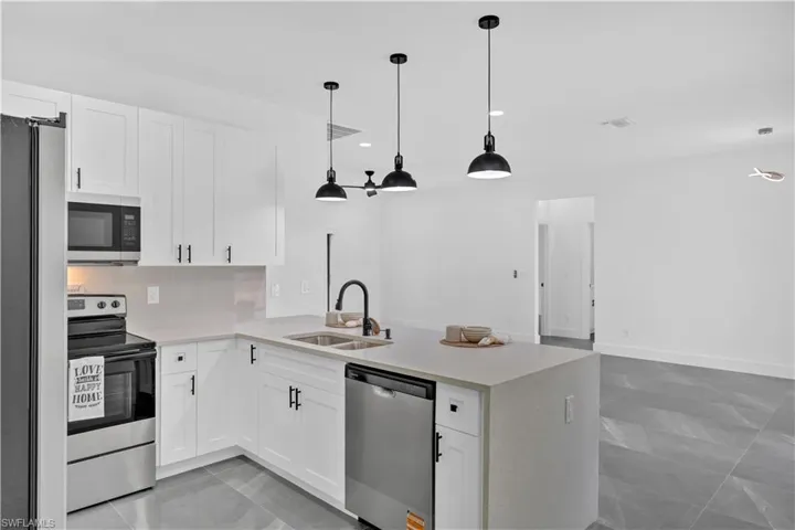 Kitchen with stainless steel appliances, white cabinetry, hanging light fixtures, a peninsula, and light stone countertops