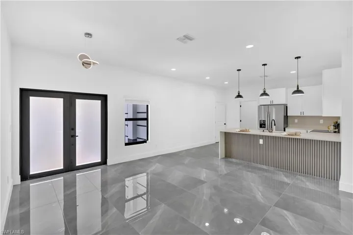 Kitchen featuring white cabinetry, french doors, stainless steel fridge with ice dispenser, light stone countertops, and decorative light fixtures