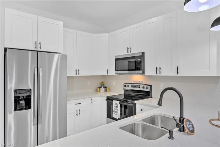 Kitchen featuring stainless steel appliances, white cabinets, light stone countertops, and decorative backsplash