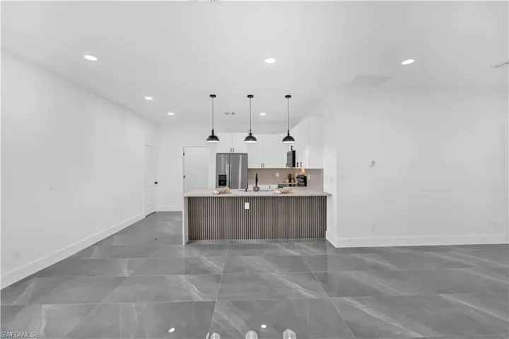 Kitchen with a peninsula, white cabinets, decorative light fixtures, stainless steel appliances, and a breakfast bar