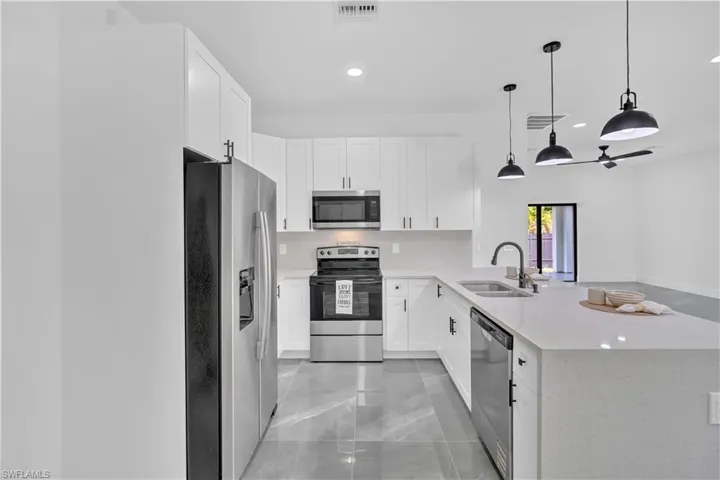 Kitchen with stainless steel appliances, white cabinets, light stone countertops, decorative light fixtures, and a peninsula