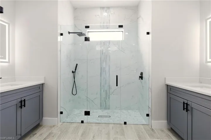 Full bath featuring two vanities, a marble finish shower, and wood tiled floors