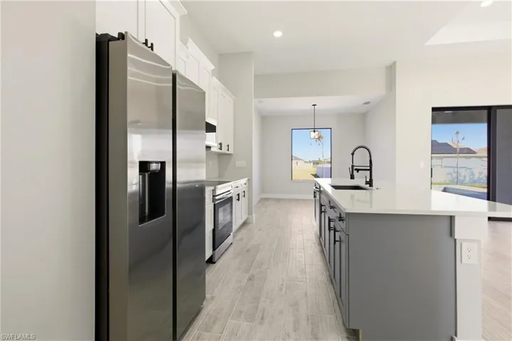 Kitchen featuring modern two-tone cabinets, black handles, appliances with stainless steel finishes, light wood-style floors, an island with sink and luxury quartz countertops, and recessed lighting.