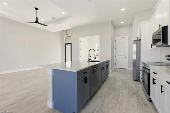 Kitchen featuring appliances with stainless steel finishes, white cabinetry, wood finish floors, recessed lighting, and a center island with sink and garbage disposal.
