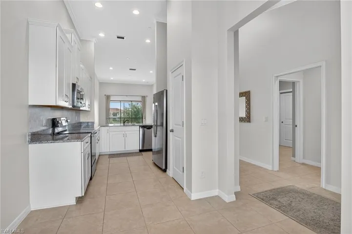 Kitchen featuring appliances with stainless steel finishes, light tile patterned floors, dark stone countertops, white cabinets, and recessed lighting