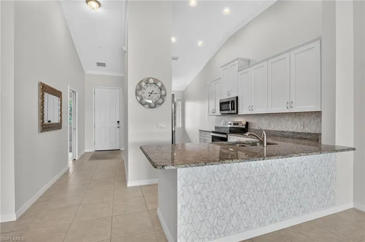 Kitchen with dark stone countertops, vaulted ceiling, appliances with stainless steel finishes, light tile patterned floors, and tasteful backsplash
