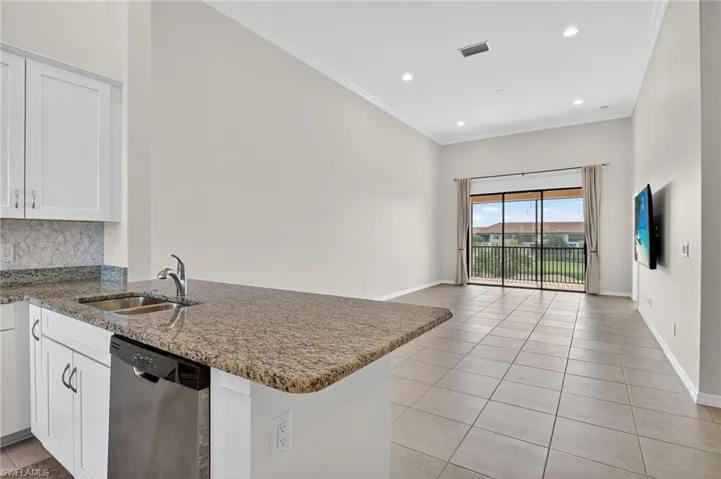 Kitchen featuring stainless steel dishwasher, a peninsula, light tile patterned flooring, white cabinetry, and stone countertops