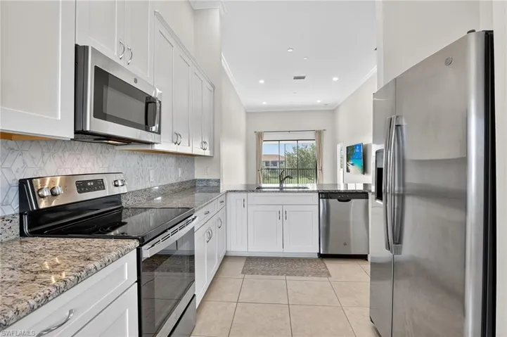 Kitchen featuring stainless steel appliances, ornamental molding, white cabinets, light stone countertops, and tasteful backsplash