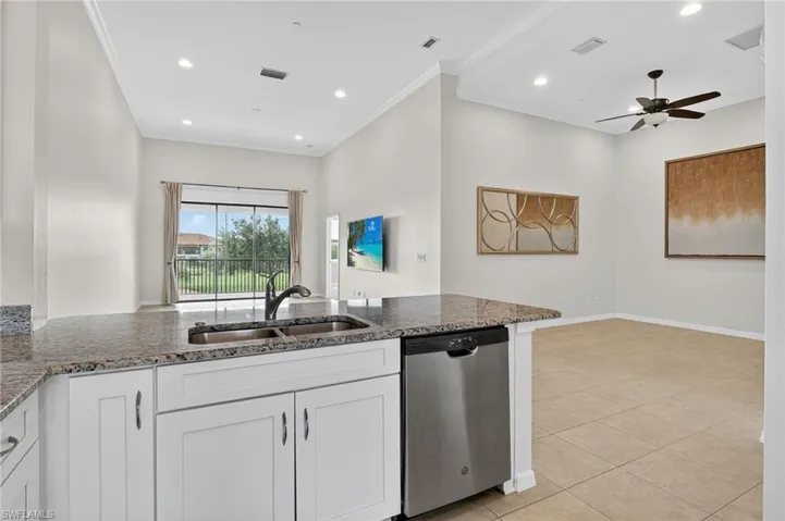 Kitchen with stainless steel dishwasher, dark stone countertops, white cabinetry, ornamental molding, and a ceiling fan